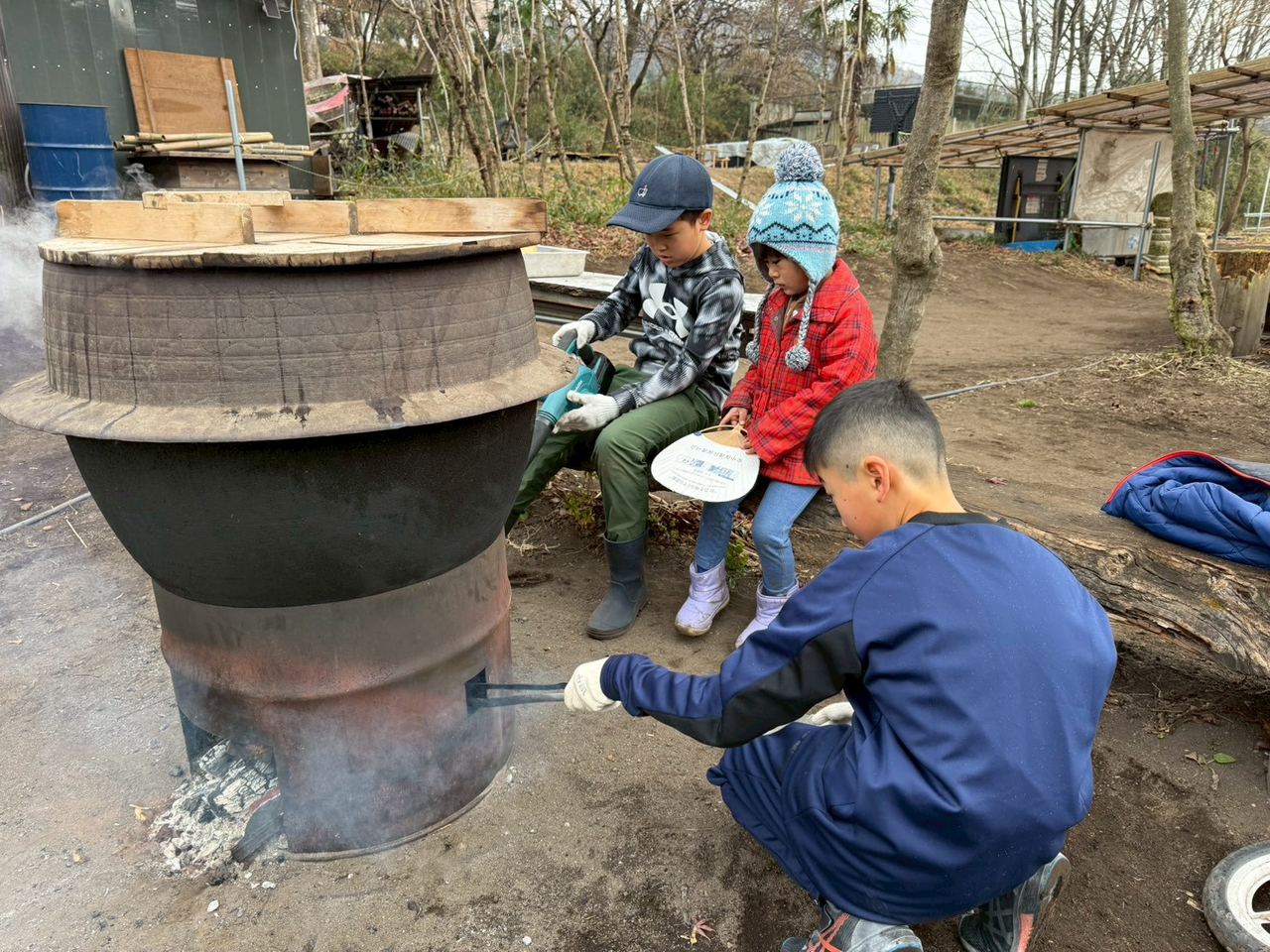 大きな鍋を囲んで火の様子を見る子どもたち