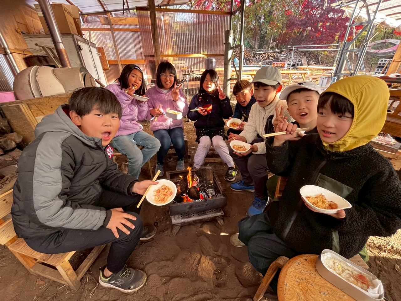 火を囲み、器を手にみんなで食事をする子どもたち